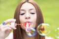 Closeup portrait of beautiful woman inflating colorful soap bubble on green background. Royalty Free Stock Photo