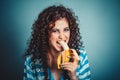 Closeup portrait beautiful woman making fun eating banana isolated on blue background wall Royalty Free Stock Photo