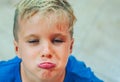 Closeup portrait boy mischievous cute blond close blue eyes, stuck out lip gesture of unwillingness, making freckles