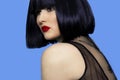 Closeup portrait of a brunette woman in black wig with make up, red lips, over blue background. Royalty Free Stock Photo