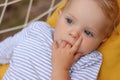 Closeup portrait of calm cute curious blonde infant girl wearing striped shirt laying in hammock outdoor, baby baby sucking