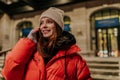 Closeup portrait of charming young woman in warm winter hat and jacket talking using holding mobile phone standing on Royalty Free Stock Photo