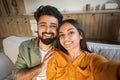 Closeup portrait of cheerful indian couple taking selfie, resting on sofa at home and smiling, posing in living room Royalty Free Stock Photo