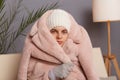 Closeup portrait of cold frozen woman wearing warm clothes and wrapped in coat sitting in room near lamp, looking at camera, needs Royalty Free Stock Photo