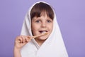 Closeup portrait of cute little girl in bath towel on her head cleaning teeth with toothbrush isolated over lilac studio Royalty Free Stock Photo