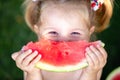 Closeup portrait of cute little girl eating watermelon on the grass in summertime Royalty Free Stock Photo