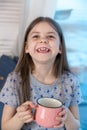 Closeup portrait of a cute little girl with a white milk mustache, pleased charming baby laughing. He holds a glass with Royalty Free Stock Photo