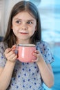 Closeup portrait of a cute little girl with a white milk mustache, pleased charming child with a smile holds a glass Royalty Free Stock Photo