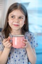 Closeup portrait of a cute little girl with a white milk mustache, pleased charming child with a smile holds a glass Royalty Free Stock Photo