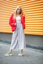 Closeup portrait of cute smiling little model girl in red jacket and glasses posing near gray corrugated striped orange gray wall Royalty Free Stock Photo