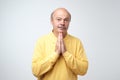 Closeup portrait of desperate mature man in yellow shirt showing clasped hands,asking for help or excuse. Royalty Free Stock Photo