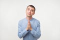 Closeup portrait of desperate young man in blue shirt showing clasped hands,asking for help or excuse. Royalty Free Stock Photo