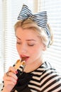 Closeup portrait of eating chocolate bar beautiful blond young woman having fun happy smiling & looking down on sun lighted window Royalty Free Stock Photo