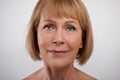 Closeup portrait of elegant mature lady with soft silky skin and nude makeup looking at camera on light background Royalty Free Stock Photo