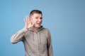 Closeup portrait of european man placing hand on ear listening carefully to gossip isolated on colored blue background Royalty Free Stock Photo