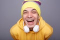 Closeup portrait of extremely happy cheerful hipster man wearing yellow hoodie and beanie hat, hearing funny joke or watching Royalty Free Stock Photo