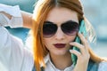 Closeup portrait of fashionable young redhead woman in sunglasses talking on cell phone outdoors in summer Royalty Free Stock Photo