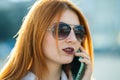 Closeup portrait of fashionable young redhead woman in sunglasses talking on cell phone outdoors in summer Royalty Free Stock Photo