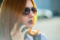 Closeup portrait of fashionable young redhead woman in sunglasses talking on cell phone outdoors in summer Royalty Free Stock Photo