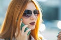 Closeup portrait of fashionable young redhead woman in sunglasses talking on cell phone outdoors in summer Royalty Free Stock Photo