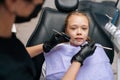 Closeup portrait of frightened cute little girl sitting in dental chair and looking at camera. Back view of female Royalty Free Stock Photo