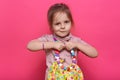 Closeup portrait of funny little girl with multicolored women`s bag in hands, has jewelry, looking at camera, wearing casual shir