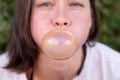 Closeup portrait of funny women, carefully inflates bubble gum, with narrowed eyes and round cheeks, outdoors.