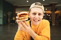 Closeup portrait of a funny young man holding a burger in his hand and looking into the camera with a shocked face. A surprised
