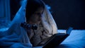 Closeup portrait of little girl lying in bed and reading book with flashlight Royalty Free Stock Photo