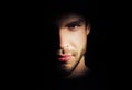 Closeup portrait of handsome man with strong look standing in dark light in studio on black background Royalty Free Stock Photo