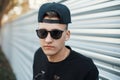 Closeup portrait of a handsome young hipster man in trendy sunglasses in a stylish black baseball cap in a shirt in the city near Royalty Free Stock Photo