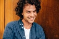 Closeup portrait of handsome young man with curly hair, smiling and looking aside, standing at modern metal building wall outdoors Royalty Free Stock Photo