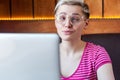 Closeup portrait of happy beautiful childish young girl with short hair in pink t-shirt and eyeglasses is sitting in cafe and