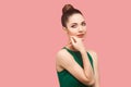 Closeup portrait of happy beautiful young woman with bun hairstyle and makeup in green dress standing touching her face and Royalty Free Stock Photo