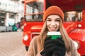 Closeup portrait of happy girl with cup of coffee standing against red bus background, looking into camera and smiling. Street Royalty Free Stock Photo