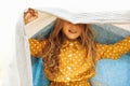 Closeup portrait of happy little blond girl smiling broadly and playing under the blanket, enjoying the summer day. Cute child Royalty Free Stock Photo