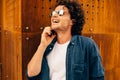 Closeup portrait of happy man standing outdoors, have a call on mobile phone. Young male with curly hair wears sunglasses talking Royalty Free Stock Photo