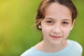 Closeup portrait of happy smiling little caucasian girl in earrings and blue blouse on warm green background Royalty Free Stock Photo