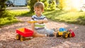 Closeup portrait of happy smiling 3 years old child boy digging sand on the playground with toy plastic truck or Royalty Free Stock Photo