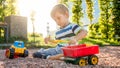 Closeup portrait of happy smiling 3 years old child boy digging sand on the playground with toy plastic truck or Royalty Free Stock Photo