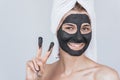 Closeup portrait of happy smiling young woman with cosmetic black clay organic mask on her face, wears black white on hair. Female Royalty Free Stock Photo