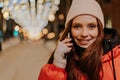 Closeup portrait of happy young woman in hat and winter jacket talking holding smartphone standing on snow city street Royalty Free Stock Photo