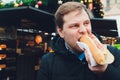 Closeup portrait of hungry man in glasses eating hot dog at outdoors background. Royalty Free Stock Photo