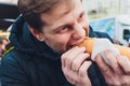 Closeup portrait of hungry man in glasses eating hot dog at outdoors background. Royalty Free Stock Photo