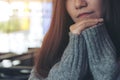 A lonely beautiful Asian woman sitting with chin resting on her hands alone in modern cafe