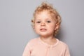 Closeup portrait of joyful confident baby girl with blonde wavy hair wearing rose shirt isolated over gray background looking at