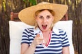 Closeup portrait of laughing young adult woman in hat and dress sitting on cozy sunbed and pointing finger to you Royalty Free Stock Photo