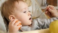 Closeup portrait of little baby boy getting messy while mother is feeding him from spoon. Concept of parenting, healthy nutrition Royalty Free Stock Photo