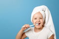 Closeup portrait of a little girl on a blue background. A child with a white towel on his head brushing his teeth. The concept of Royalty Free Stock Photo