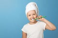 Closeup portrait of a little girl on a blue background. A child with a white towel on his head brushing his teeth. The concept of Royalty Free Stock Photo
